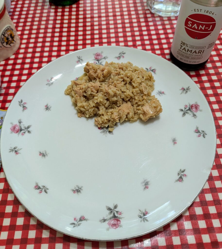 A rice and chicken dish on a plate, with a bottle of soy sauce nearby