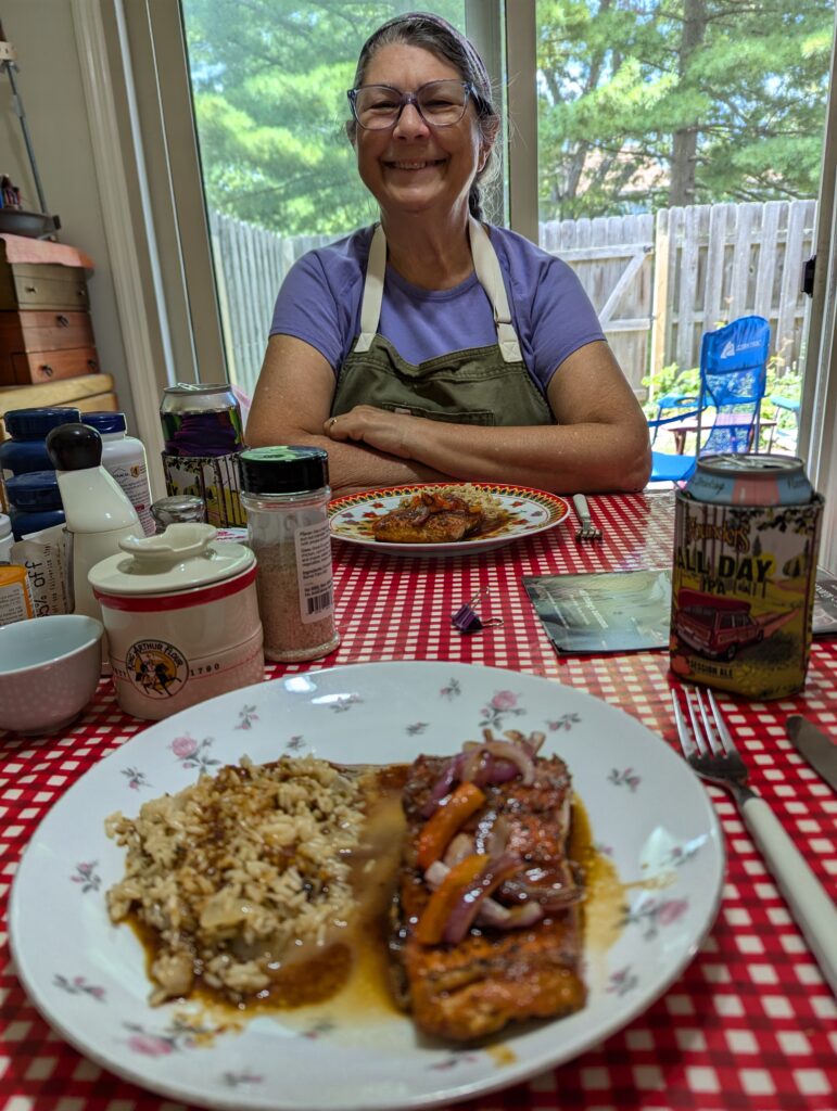 Jackie across from a table set with two servings of salmon, rice, and sauteed vegetables