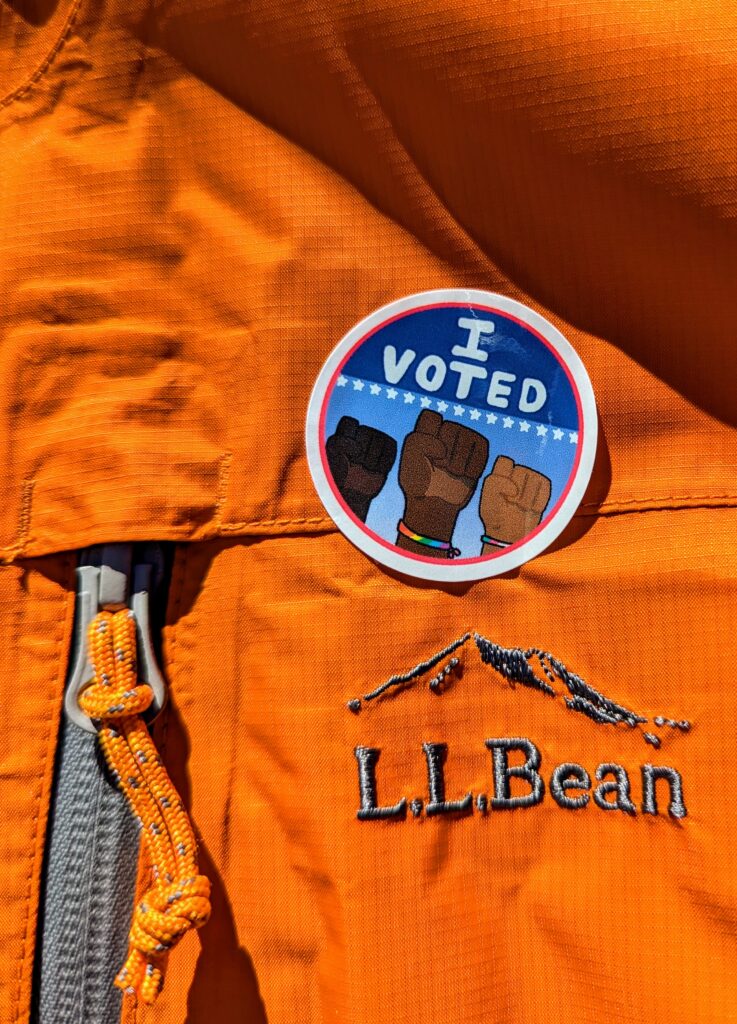 Detail of a raincoat with an "I voted" sticker next to the zipper pull, just aboven an L.L Bean logo