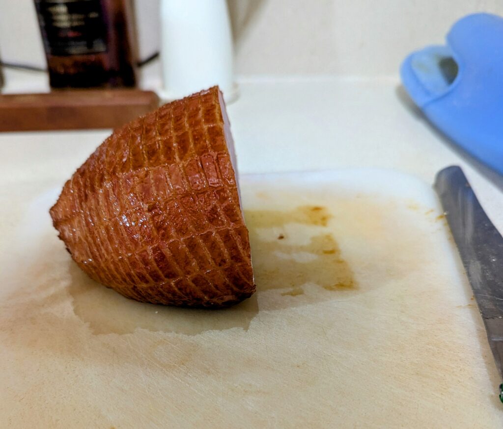 Half of a small ham, sitting on a cutting board with just a bit of a slicing knife visible